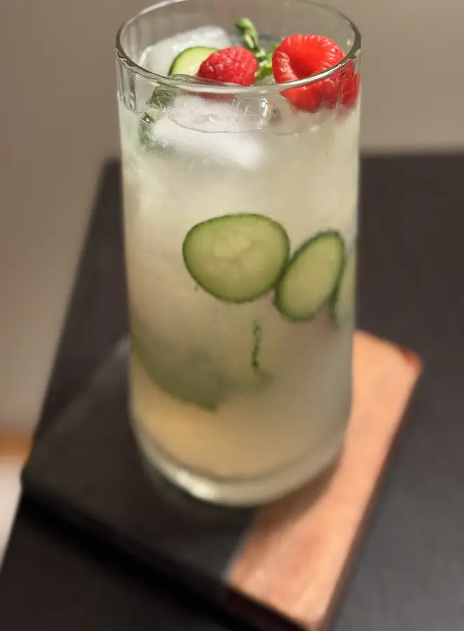 A tall cocktail with cucumber and raspberries