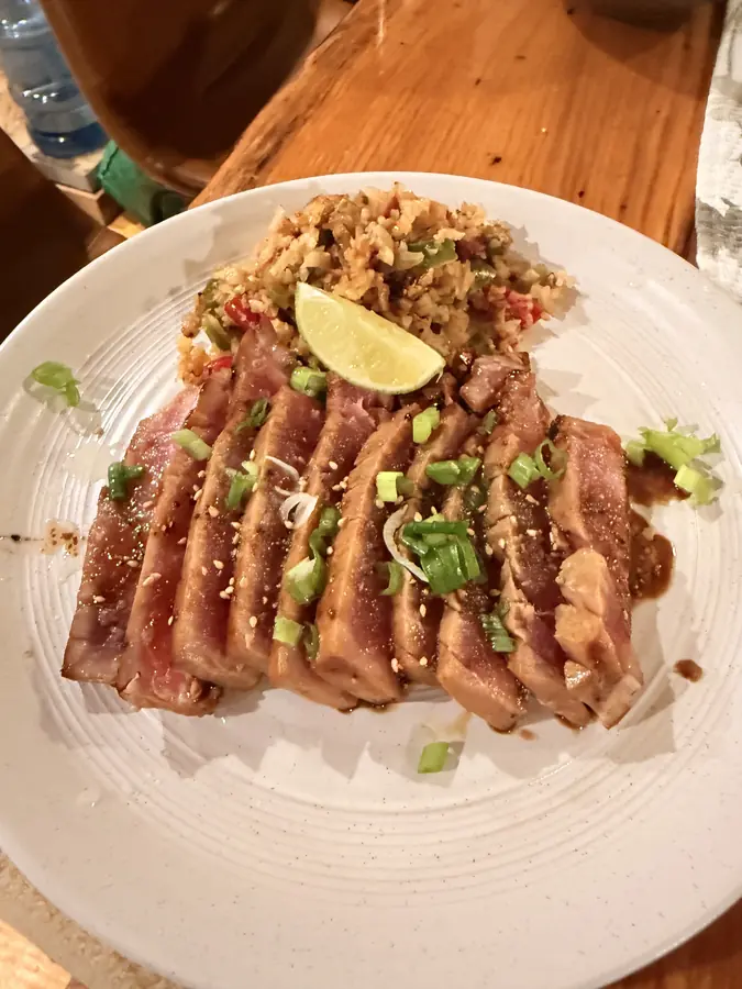 Sliced seared duck breast fanned over rice on a white plate