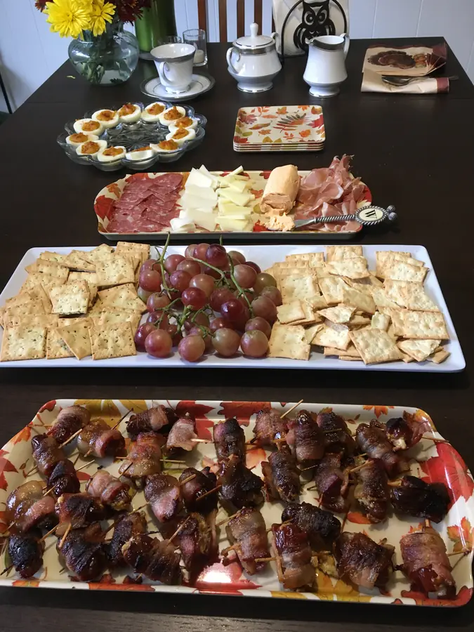 Three long platters of charcuterie, cheese, crackers and bacon-wrapped dates