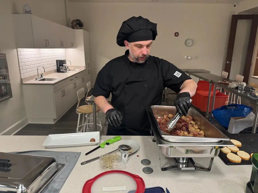 A chef in blacks plating canapes at a stainless kitchen counter