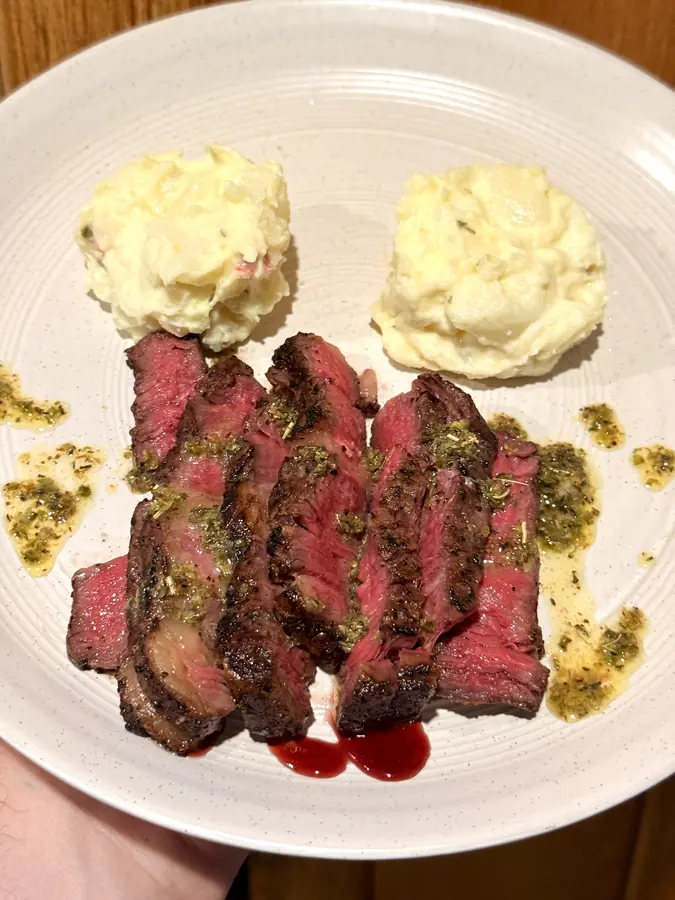 Sliced medium-rare steak with chimichurri and two quenelles of mashed potato