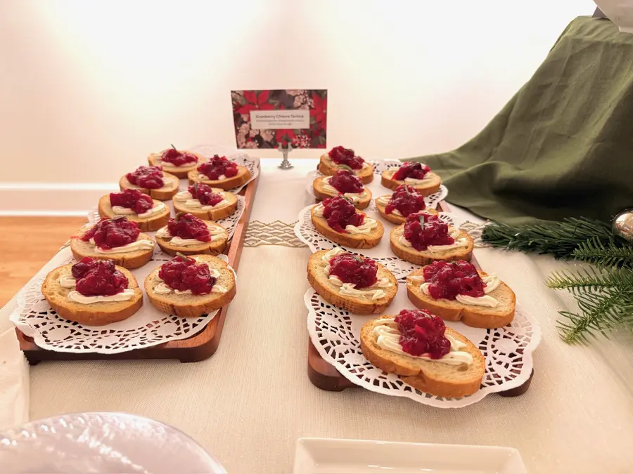Rows of cranberry tartlets on doilies beside a green table drape