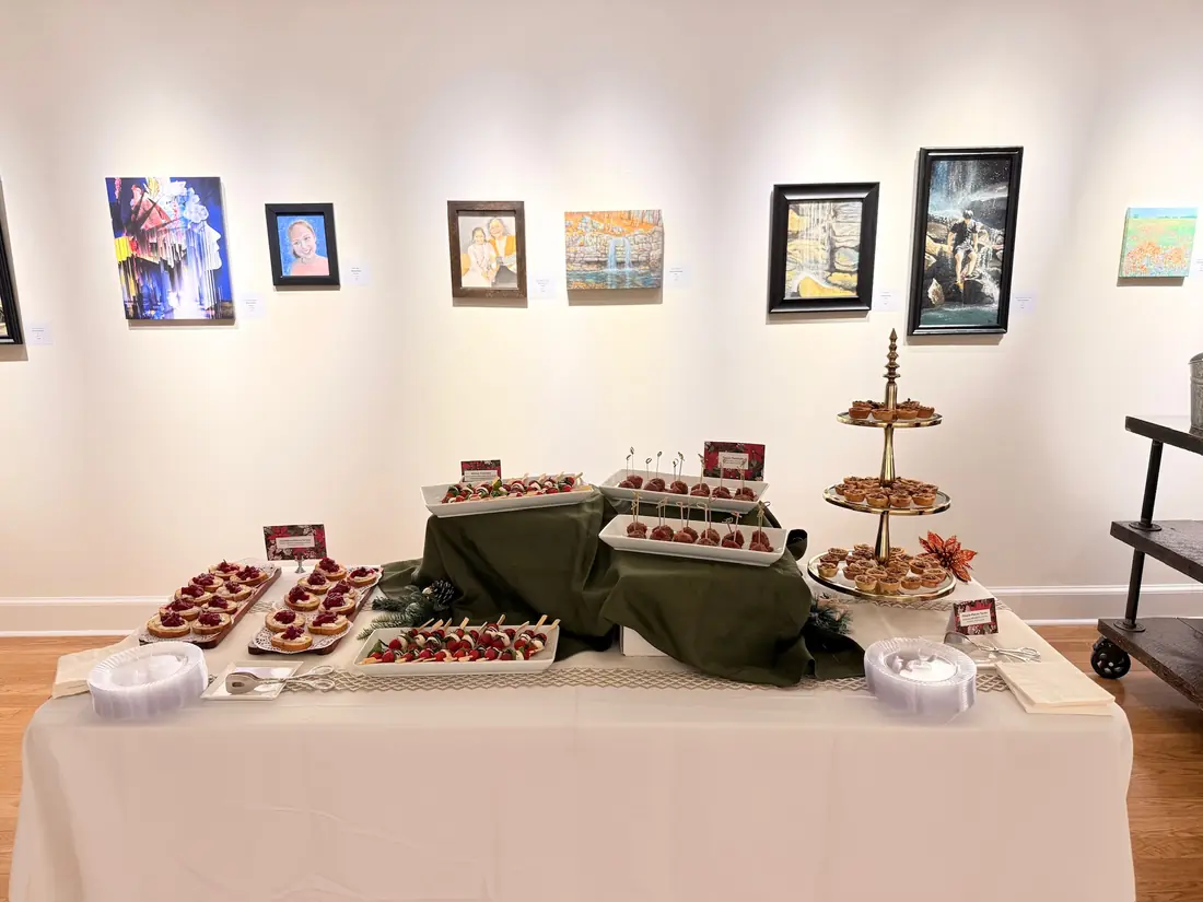 A long reception table of canapes on tiered stands against a gallery wall hung with paintings