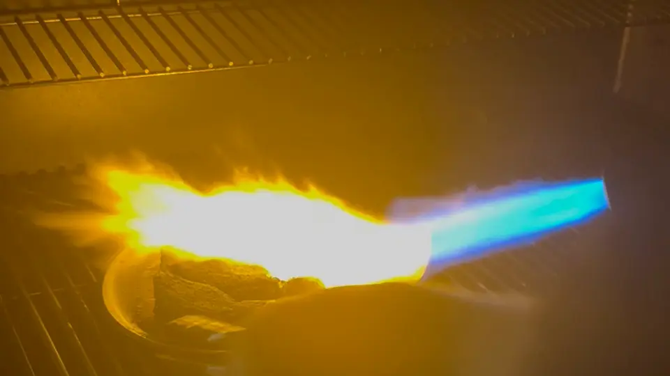 A blowtorch searing a steak on a grill grate at night